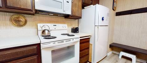 A compact kitchen with white appliances, wooden cabinets, and a small step stool.