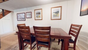 A dining area with a wooden table and four chairs, framed pictures on the wall, and a staircase to the left. - Sierra Manors 75 Cozy and Comfy Condo, On the Shuttle Route by RedAwning (Mammoth Lakes)