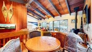 A cozy room with wooden beams, a large window, and a wooden table with chairs. - Mammoth West 143 Quiet Condo With Amazing Mountain Views and A Short Walk to Canyon Lodge by RedAwning (Mammoth Lakes)
