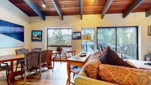 A cozy interior with a dining area, a sofa with patterned cushions, and large windows offering a view of the outdoors. - Mammoth West 143 Quiet Condo With Amazing Mountain Views and A Short Walk to Canyon Lodge by RedAwning (Mammoth Lakes)