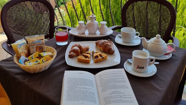 Mesa de varanda posta com um livro, doces e um bule, com vista para a paisagem urbana.