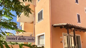 Entrada de hotel com uma placa indicando "Hotel delle Isole", plantas em vasos e céu claro.