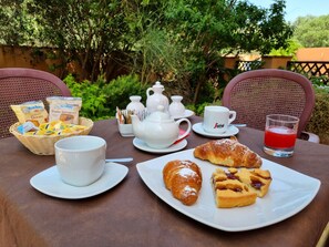 A breakfast setup with croissants, a plate of pastries, a teapot, cups, and a glass of red juice on a table.