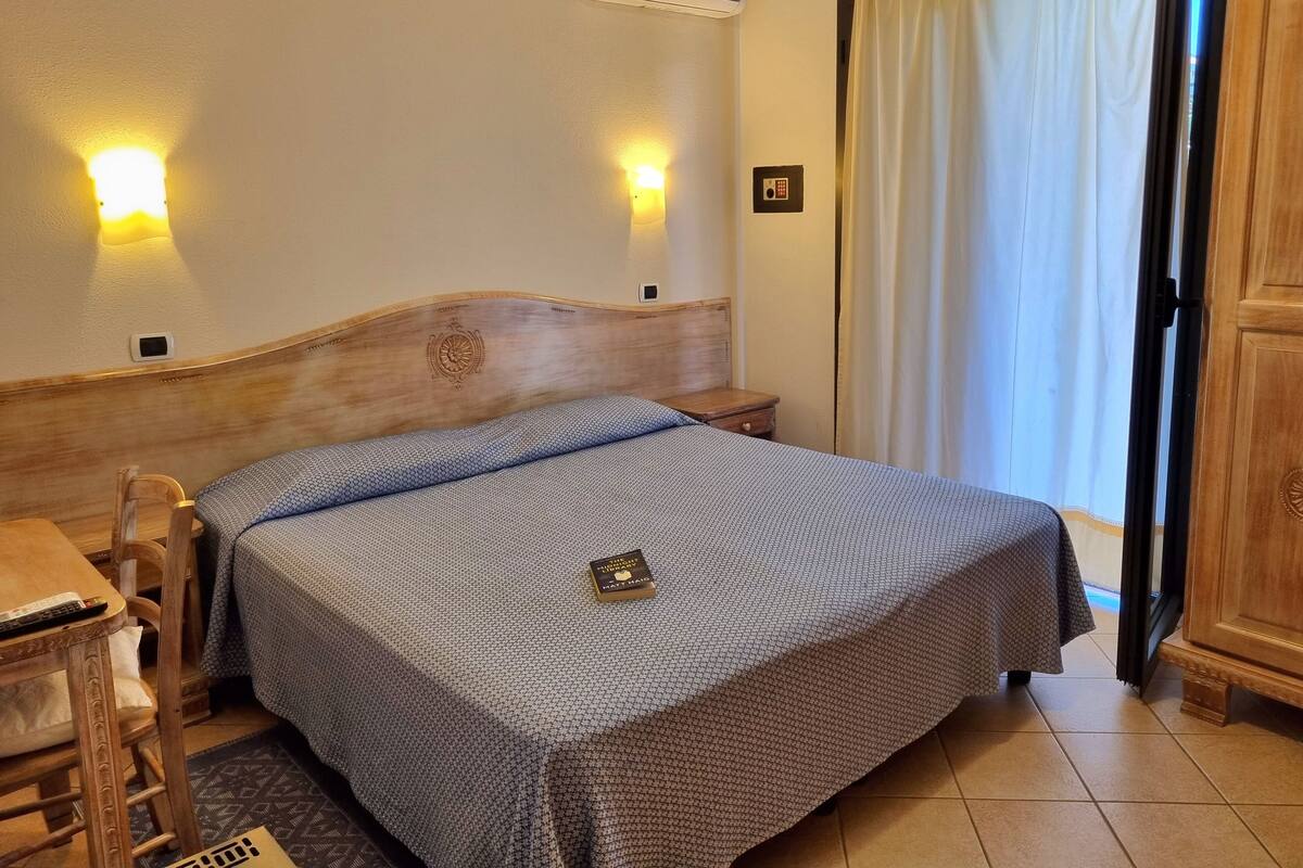 Une chambre d’hôtel avec une tête de lit en bois, un lit avec une literie à motifs, une table de chevet avec une télécommande et une petite table de nuit.