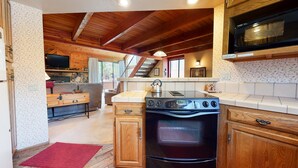 Une cuisine dotée de meubles en bois, d’une cuisinière, d’un four à micro-ondes et d’un coin repas comprenant un canapé et une table.