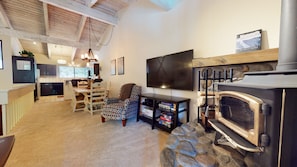Un salón acogedor con chimenea de piedra, un televisor montado en la pared y una zona de comedor con muebles de madera.