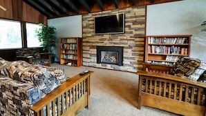 Una sala de estar con chimenea de piedra, un televisor de pantalla plana montado encima y dos estanterías llenas de libros.