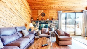 Un salon chaleureux avec une cheminée en pierre, des murs en bois et une grande fenêtre.