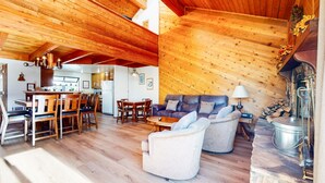 Un intérieur de chalet chaleureux comprenant un coin repas, un salon avec un canapé et des fauteuils, et une cheminée.