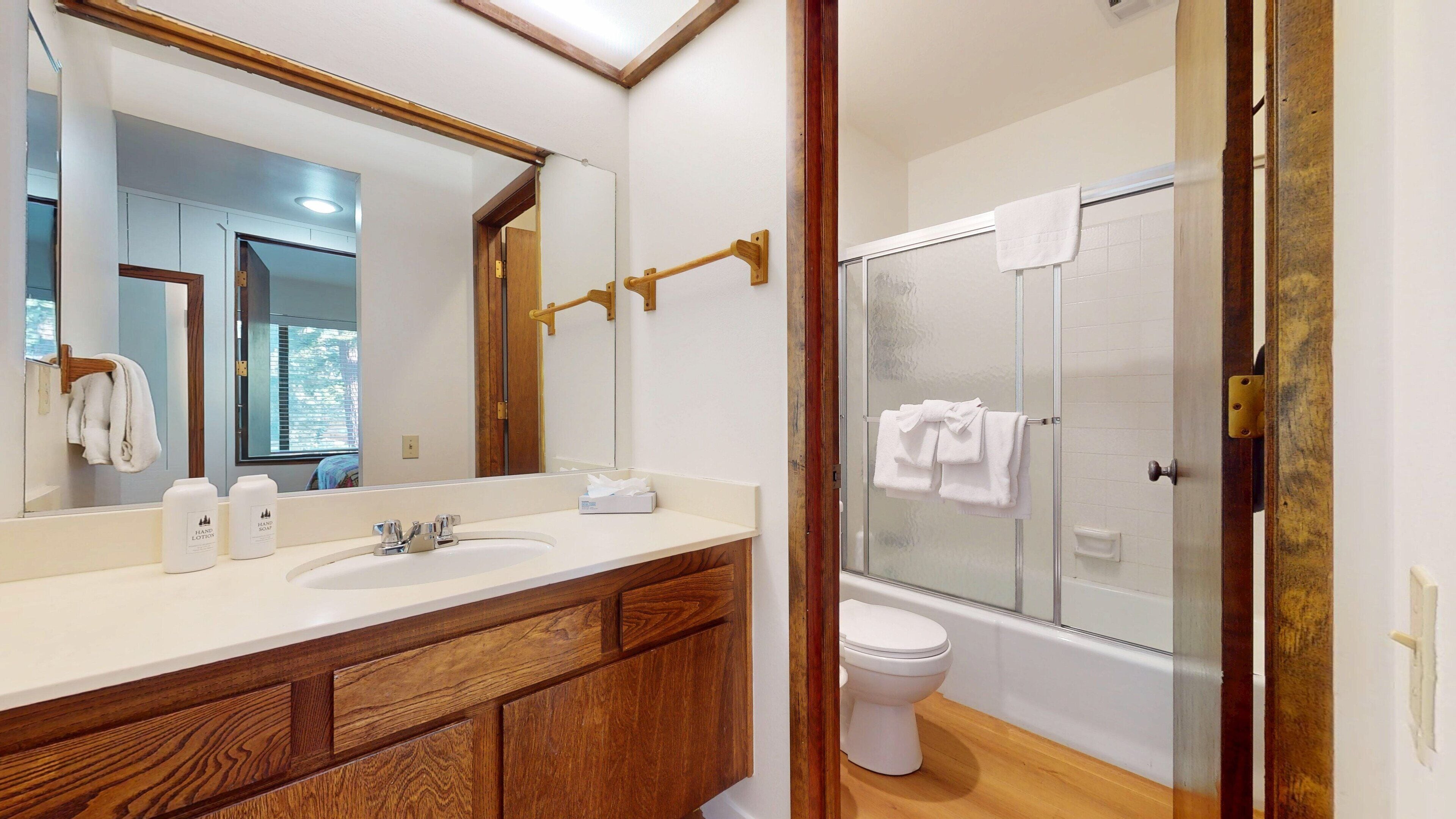 A modern bathroom with a wooden vanity, a large mirror, a glass shower enclosure, and a white toilet.