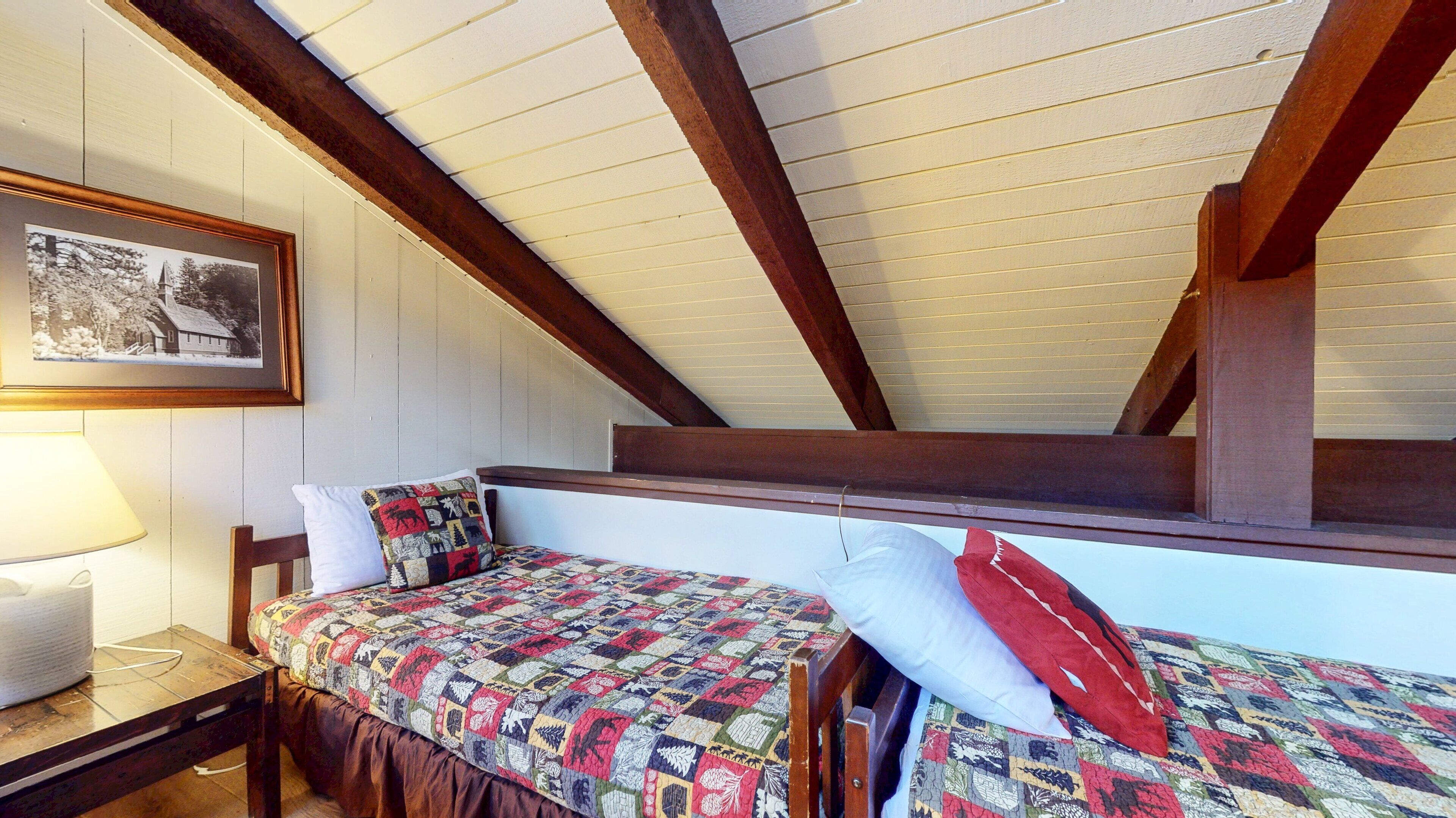 A cozy attic bedroom with a wooden ceiling, a bed with a colorful quilt, a white pillow, and a framed photo on the wall.