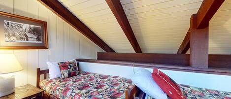 A cozy attic bedroom with a wooden ceiling, a bed with a colorful quilt, a white pillow, and a framed photo on the wall.