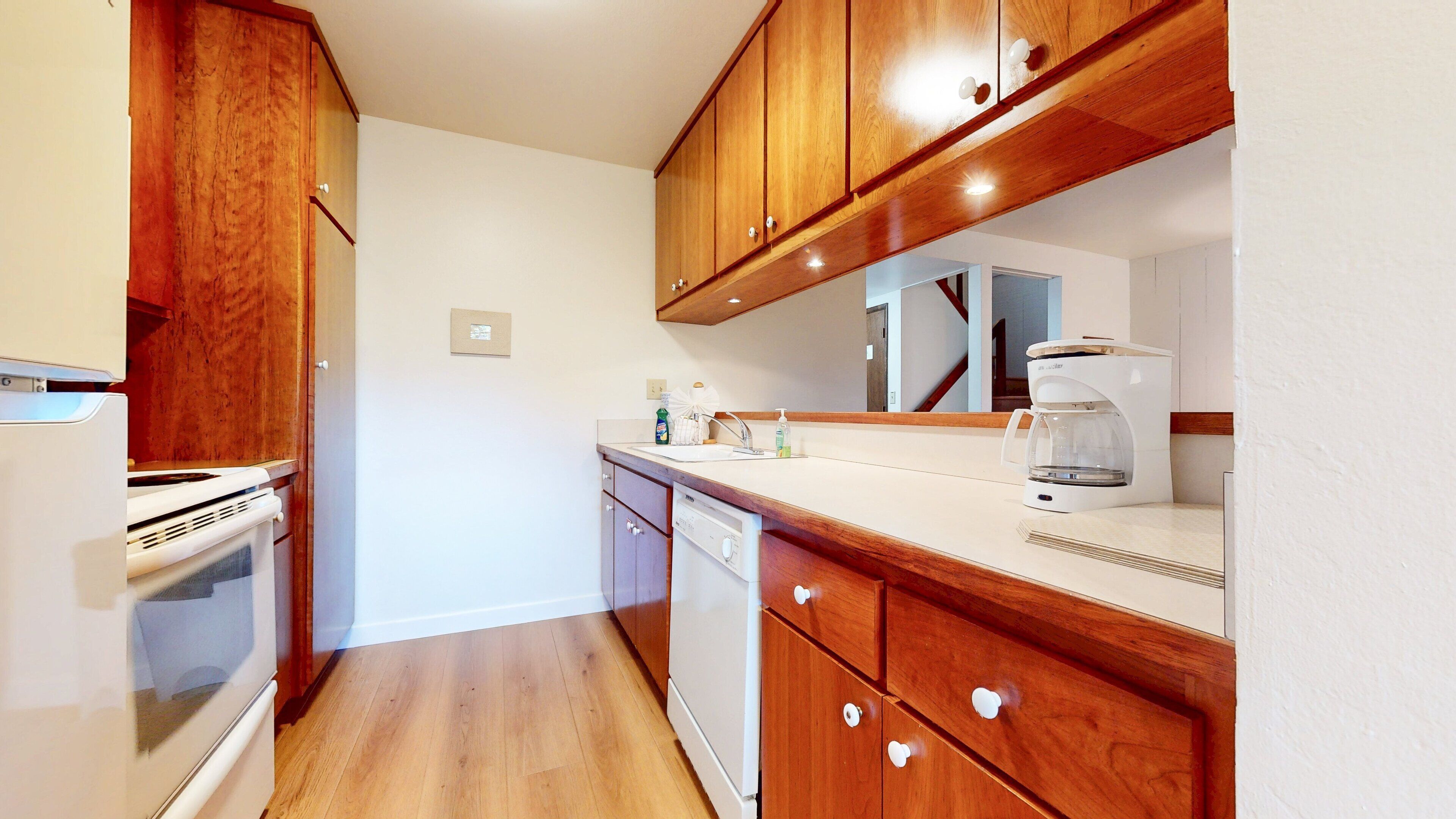A kitchen with wooden cabinets, a white countertop, a coffee maker, and a dishwasher.