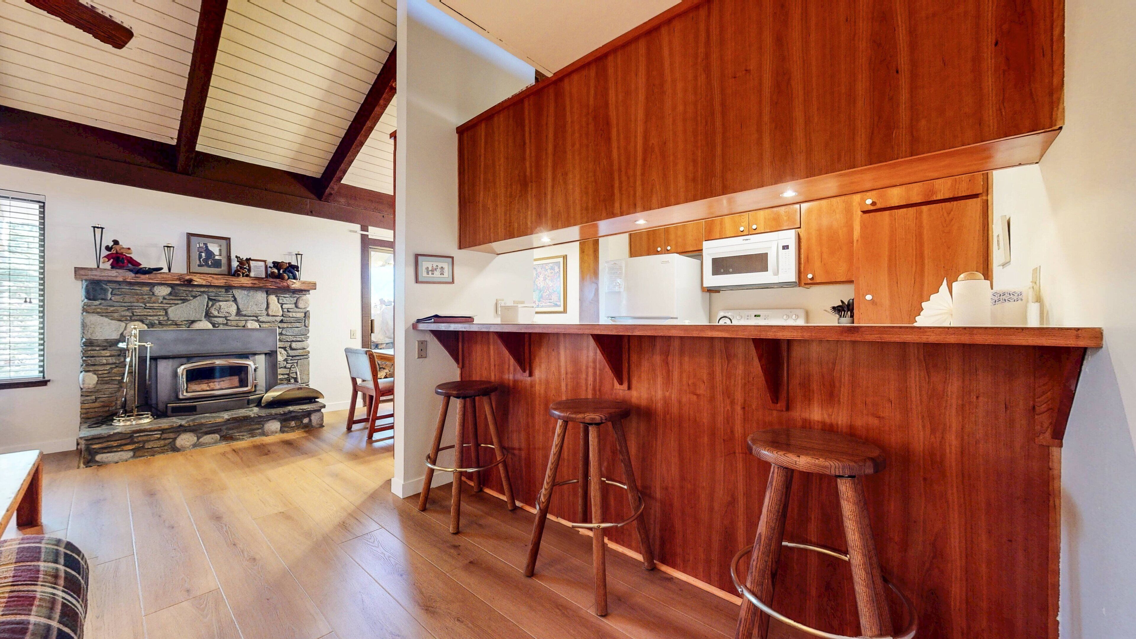 A kitchen with wooden cabinets, a stone fireplace, and a bar area with stools.