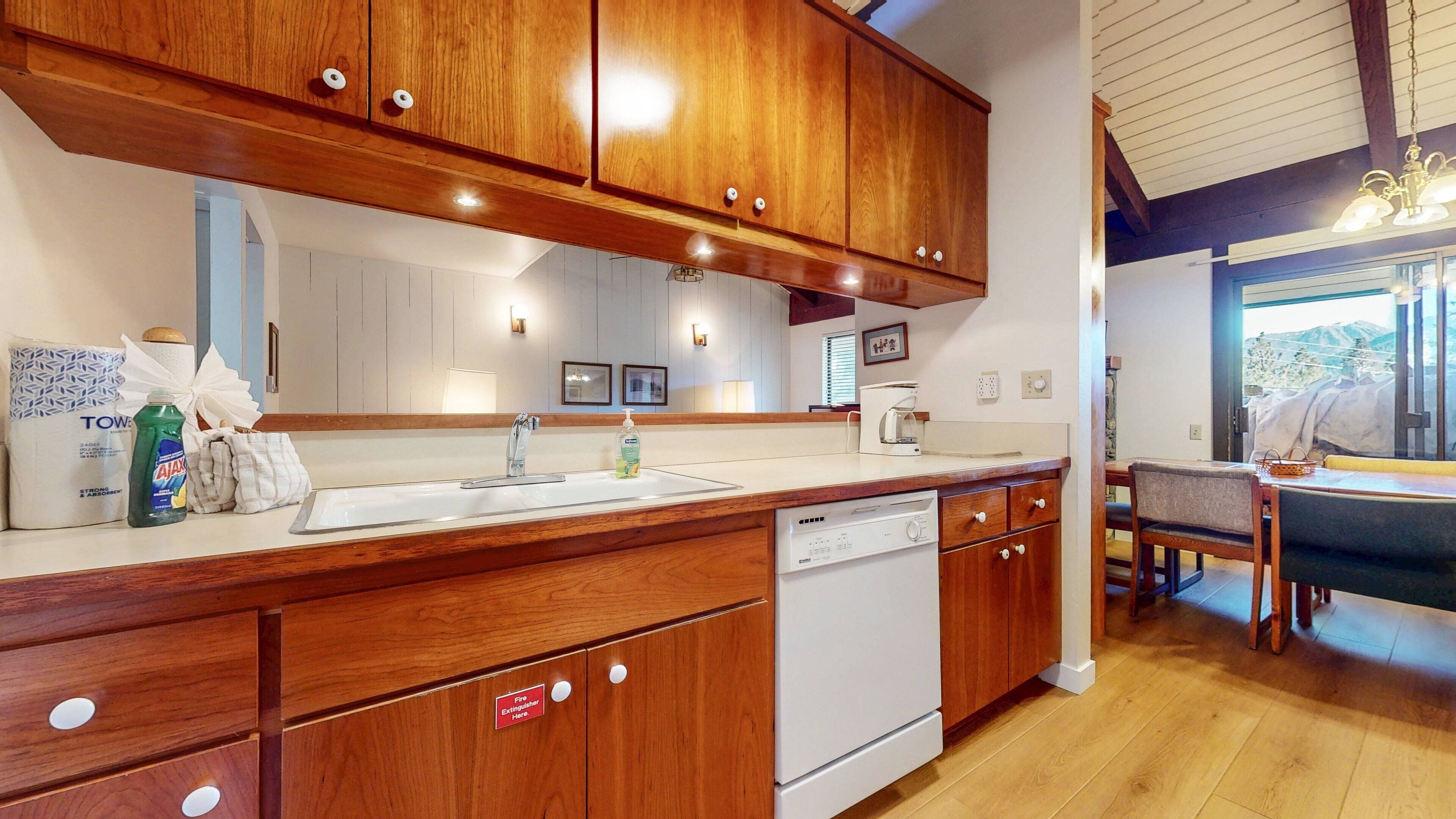 A kitchen with wooden cabinets, a white sink, and a dishwasher. There is a window with a view of the outdoors.
