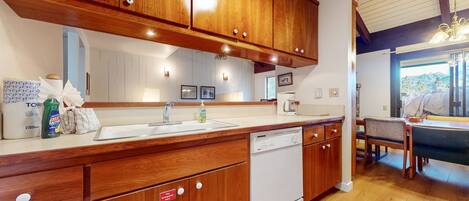 A kitchen with wooden cabinets, a white sink, and a dishwasher. There is a window with a view of the outdoors.
