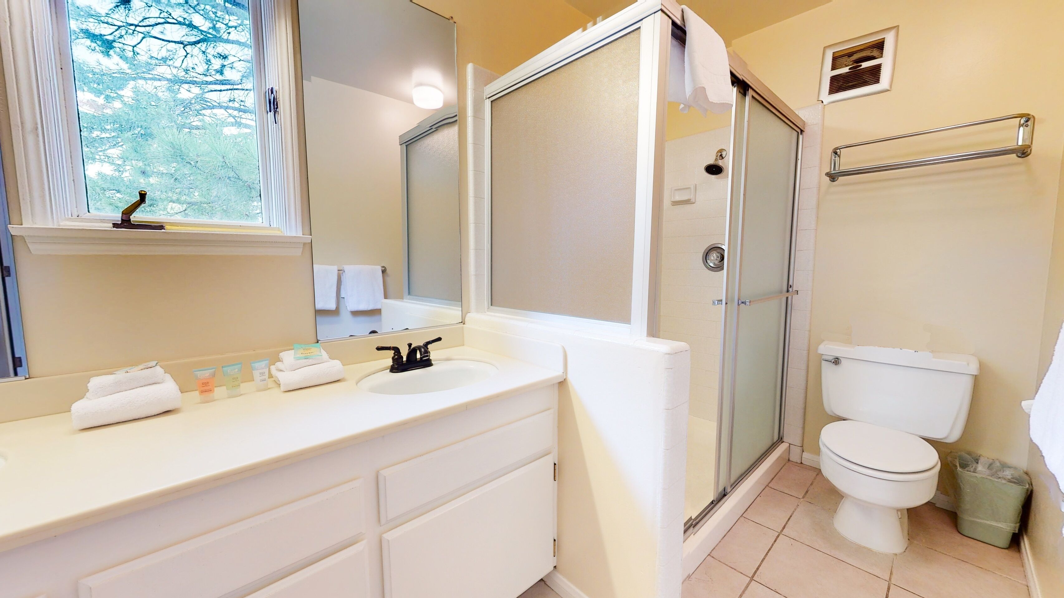 A bathroom with a white sink, mirror, and toilet. There is a shower area with a glass door and a towel rack.