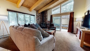 Una sala de estar acogedora con chimenea de piedra, ventanas amplias, un sofá y un televisor sobre un mueble de madera.