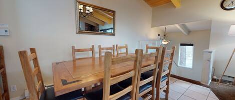 A dining area with a wooden table and chairs, a mirror on the wall, and a chandelier.