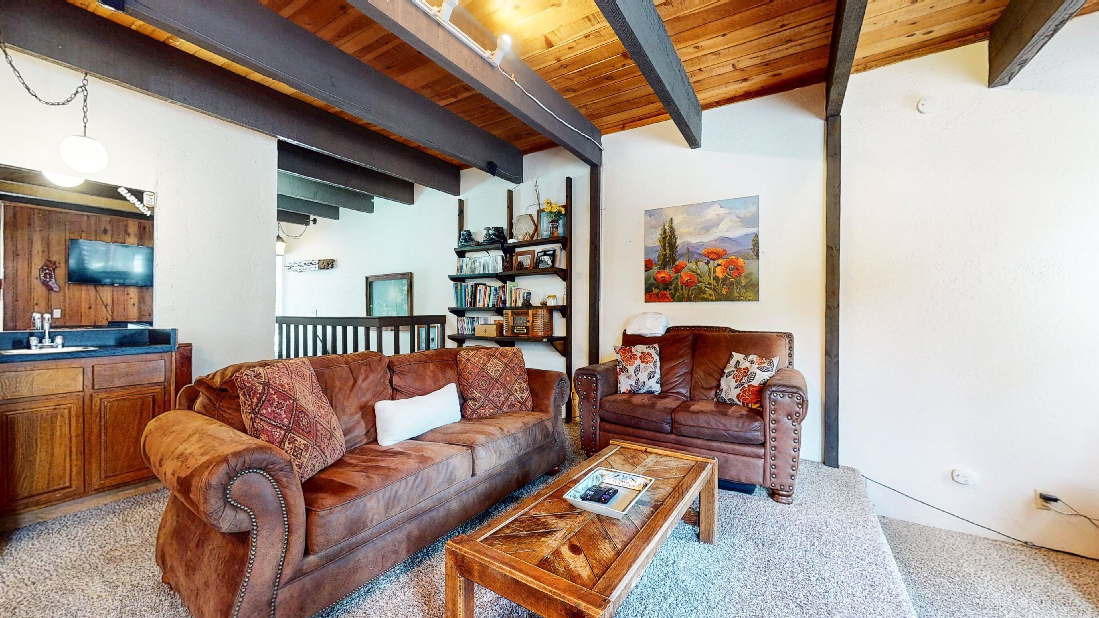A cozy living room with a leather sofa, a wooden coffee table, and a bookshelf filled with books and decorative items.