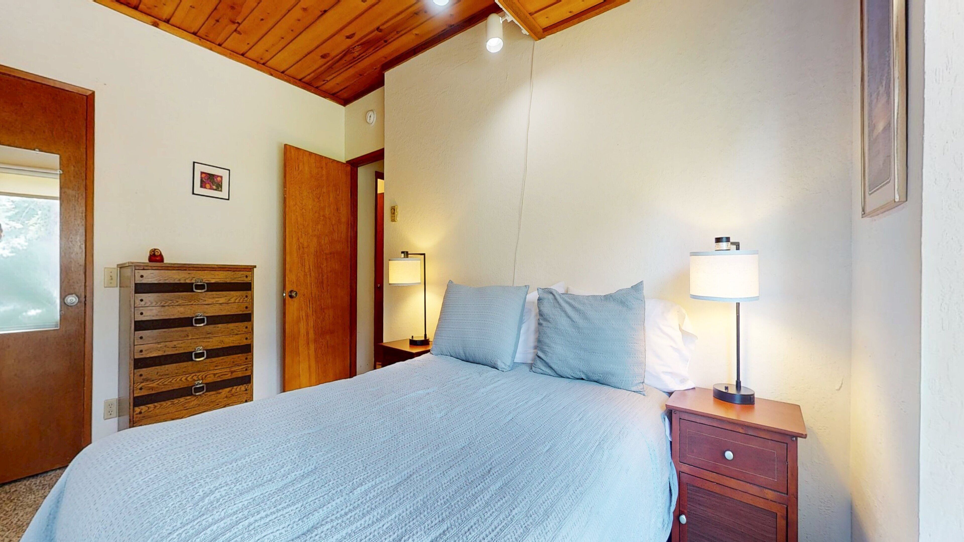 A bedroom with a bed, wooden dresser, bedside lamps, and a door.
