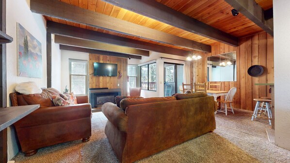 A cozy living room with a fireplace, leather sofas, and a dining area with wooden furniture.