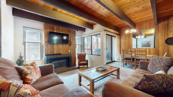 A cozy living room with a fireplace, a television, and a dining area with wooden furniture.