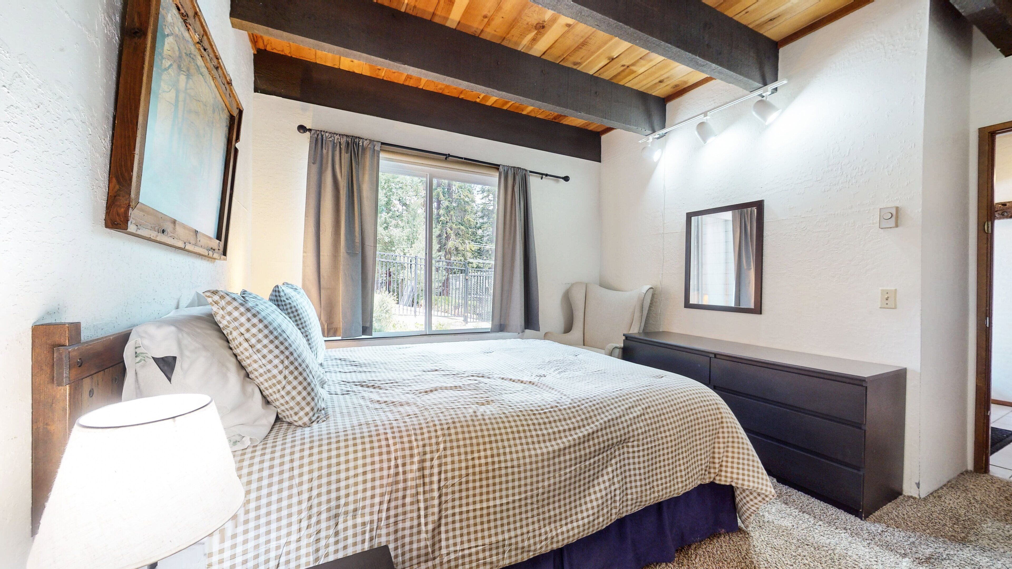 A bedroom with a bed, bedside table, lamp, and a window with curtains.