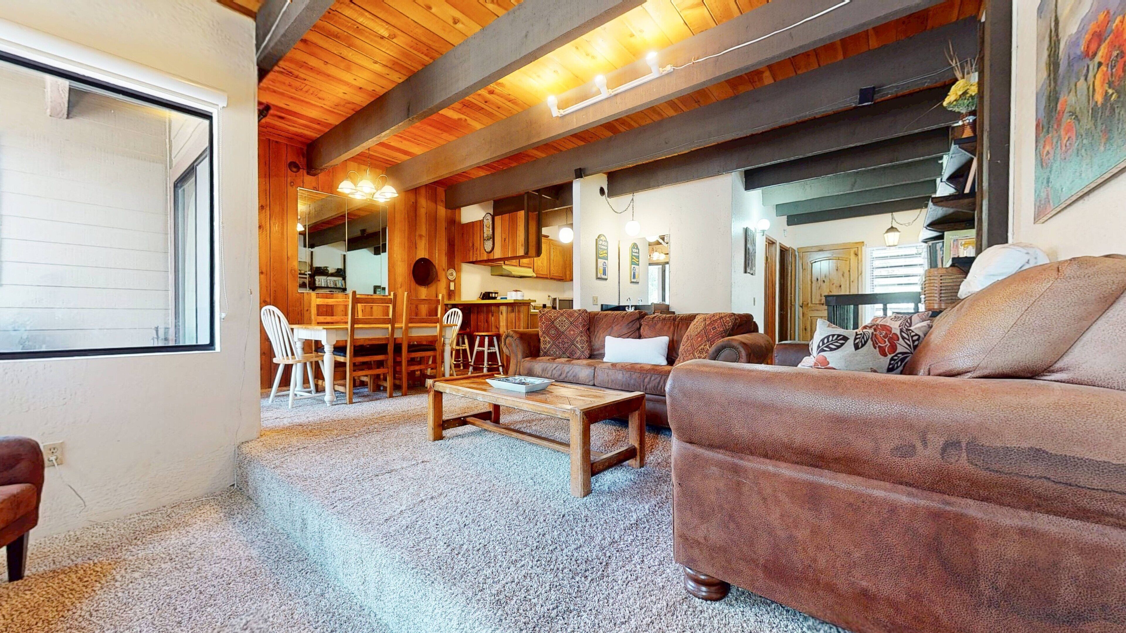 A cozy living room with a wooden ceiling, a sofa, a coffee table, and a dining area with chairs and a table.