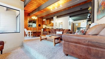 A cozy living room with a wooden ceiling, a sofa, a coffee table, and a dining area with chairs and a table.