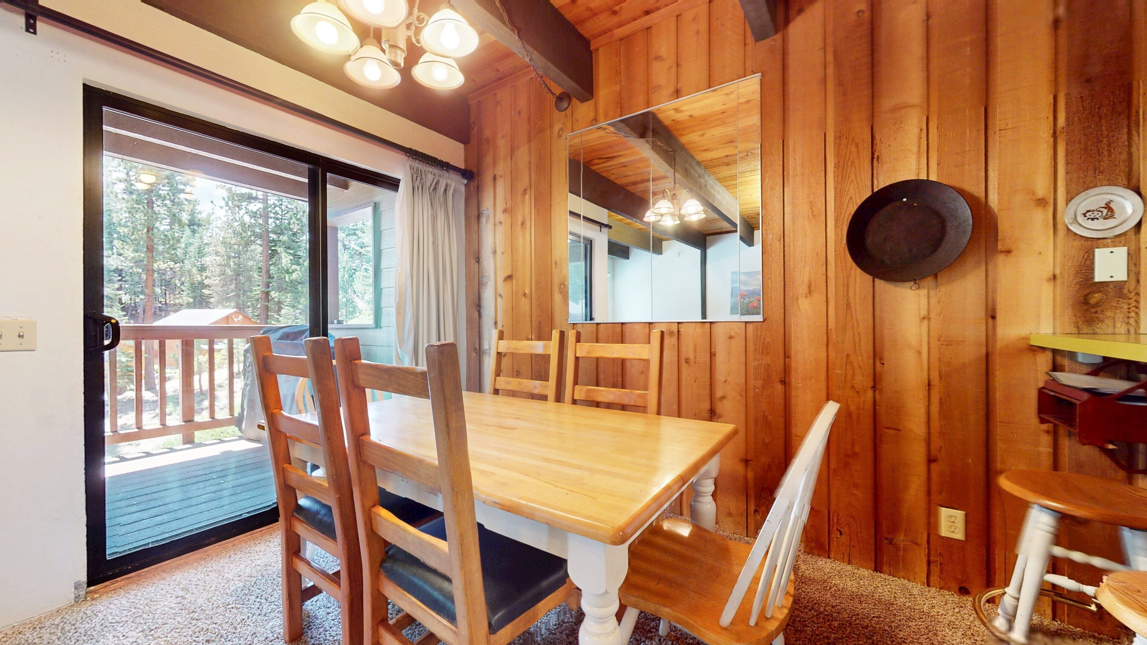 A wooden interior with a dining table, chairs, a mirror, and a view through a glass door.