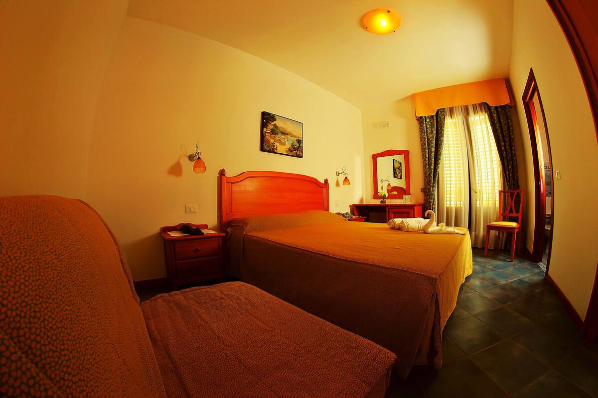 Une chambre d’hôtel avec deux lits, une table de chevet, un bureau, une chaise, un miroir et un tableau au mur.