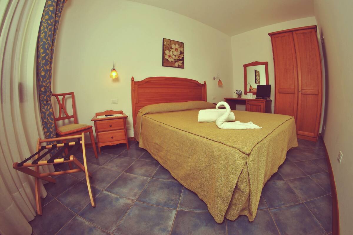 Une chambre à coucher comprenant un lit, une chaise, une table de chevet, une commode, un miroir et un luminaire fixé au mur.