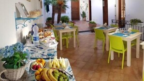A dining area with tables and chairs, a buffet with fruits and snacks, and a view of the outside. - Hotel La Meridiana (San Vito Lo Capo)