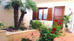 A courtyard with potted plants, a bench, and a window with wooden shutters. - Hotel La Meridiana (San Vito Lo Capo)