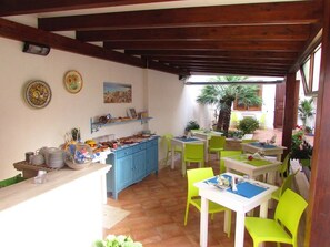 Un espace repas avec des tables et des chaises, un coin cuisine avec des placards et une vue sur l’extérieur.