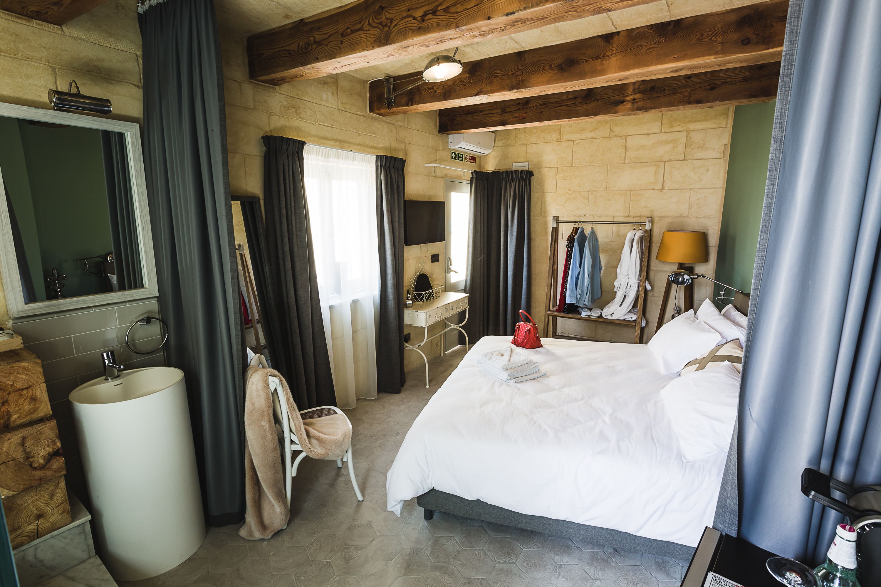A hotel room with a large bed, a desk, a chair, a sink, and a mirror.
