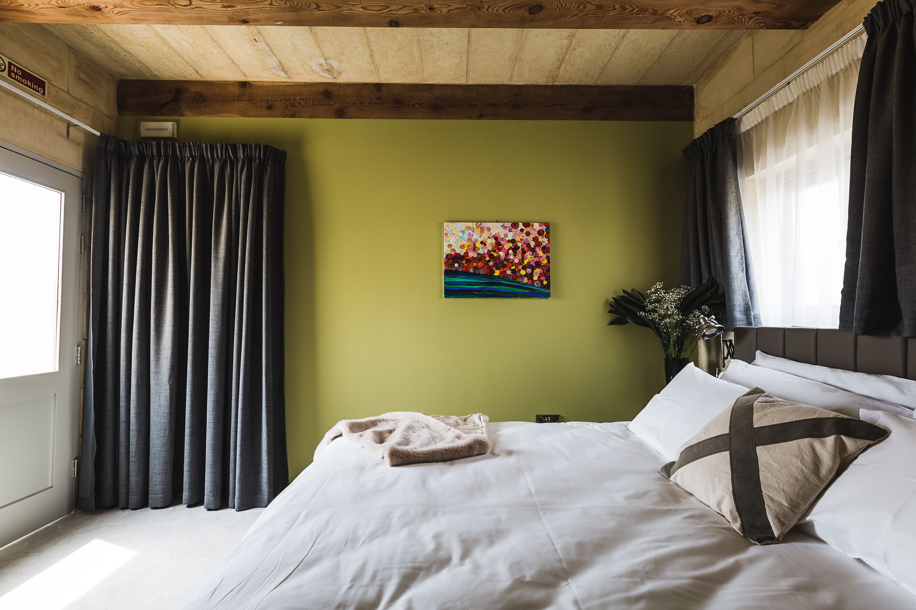 A bedroom with a bed, a painting, and curtains.