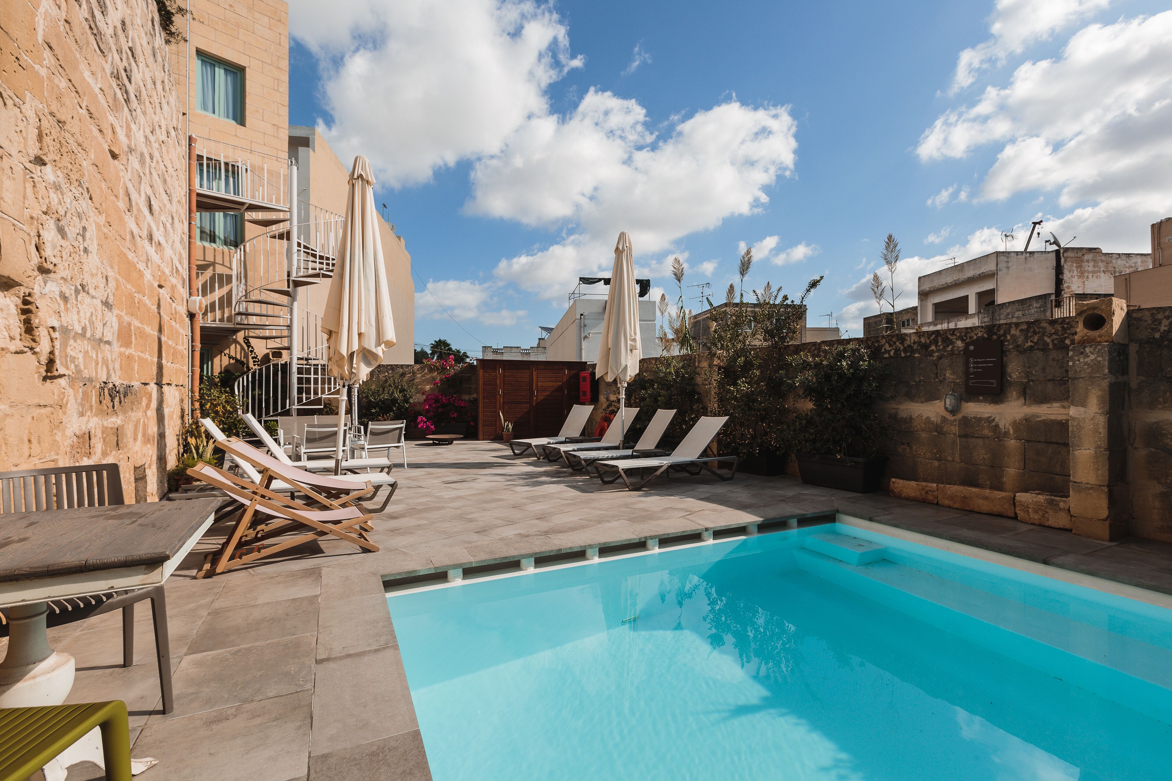 A swimming pool with lounge chairs and umbrellas, a staircase, and a view of the sky.