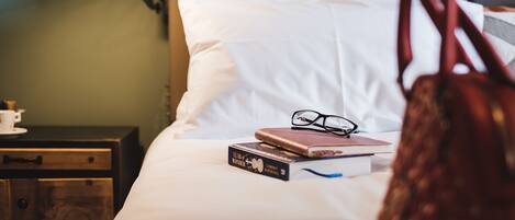 A neatly made bed with a pillow, a bedside lamp, a book, and a pair of glasses.
