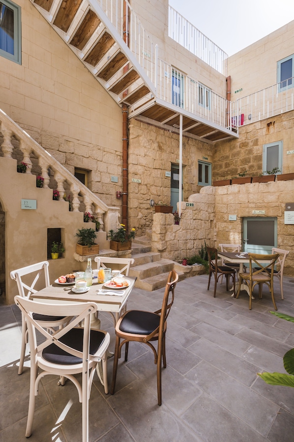 A stone building with a staircase leading to a balcony. There are outdoor tables and chairs set up for dining.
