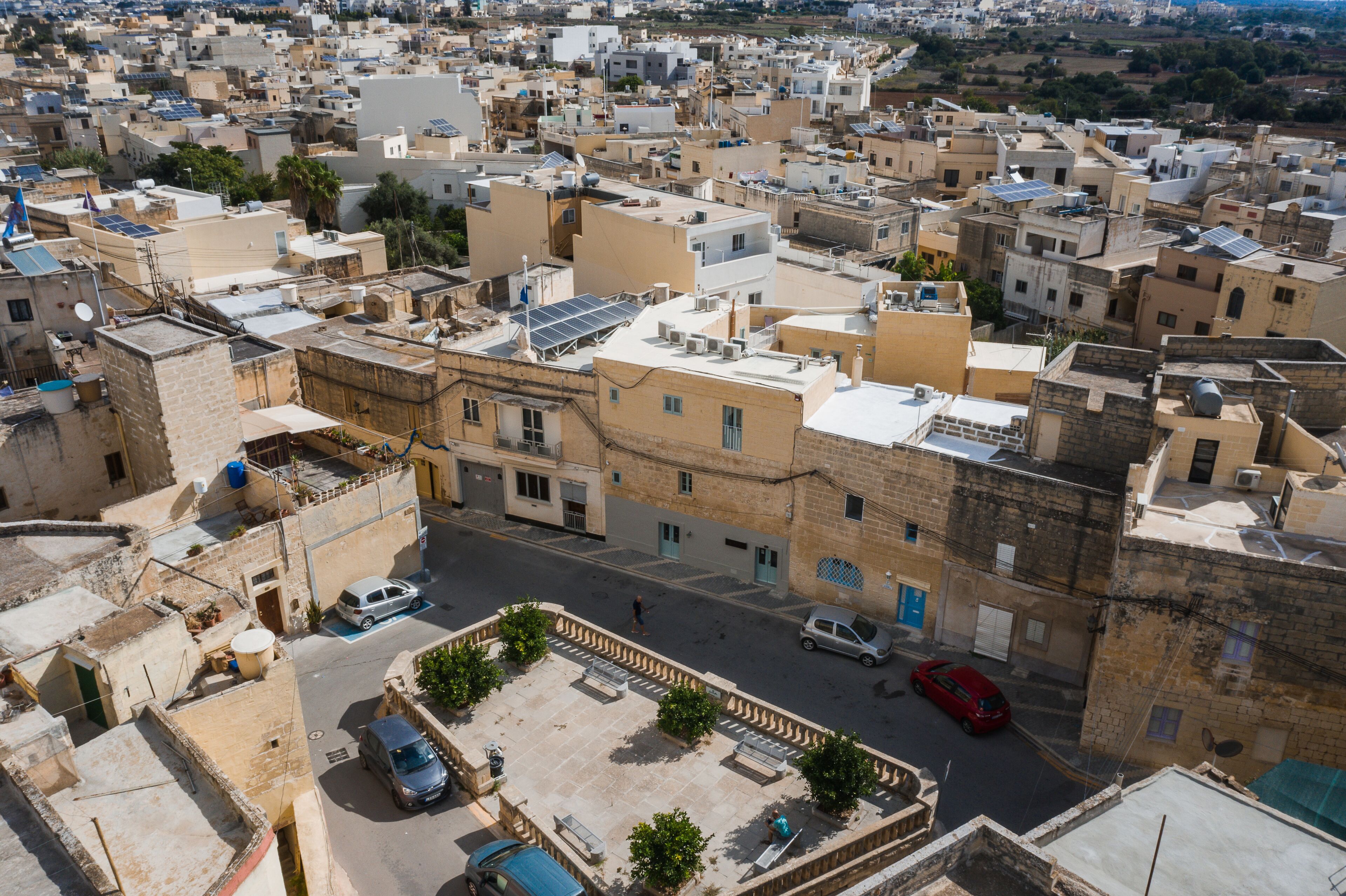 An aerial view of a densely packed urban area with closely built structures, narrow streets, and a few visible vehicles.