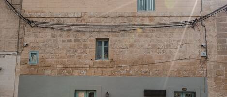 Un bâtiment à deux étages, doté d’une façade de couleur claire, de deux fenêtres bien visibles avec des encadrements bleu clair, et d’une porte avec un encadrement bleu clair.