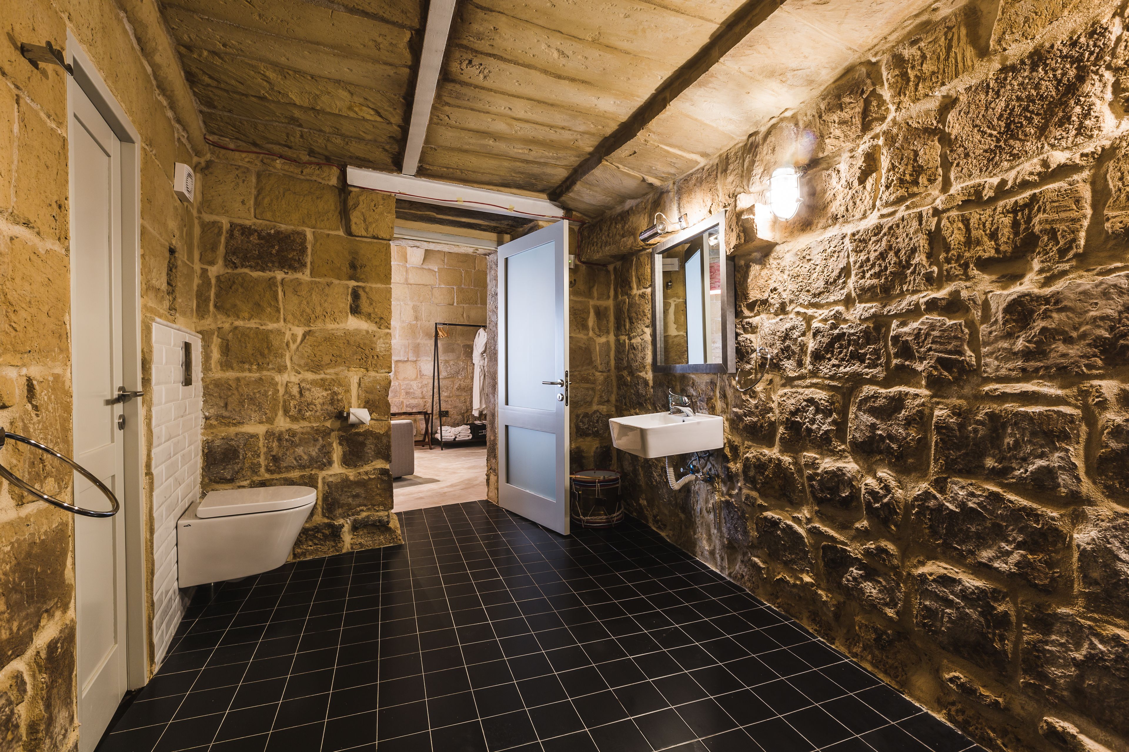 Bagno con pareti in pietra, dotato di toilette, lavandino e specchio.