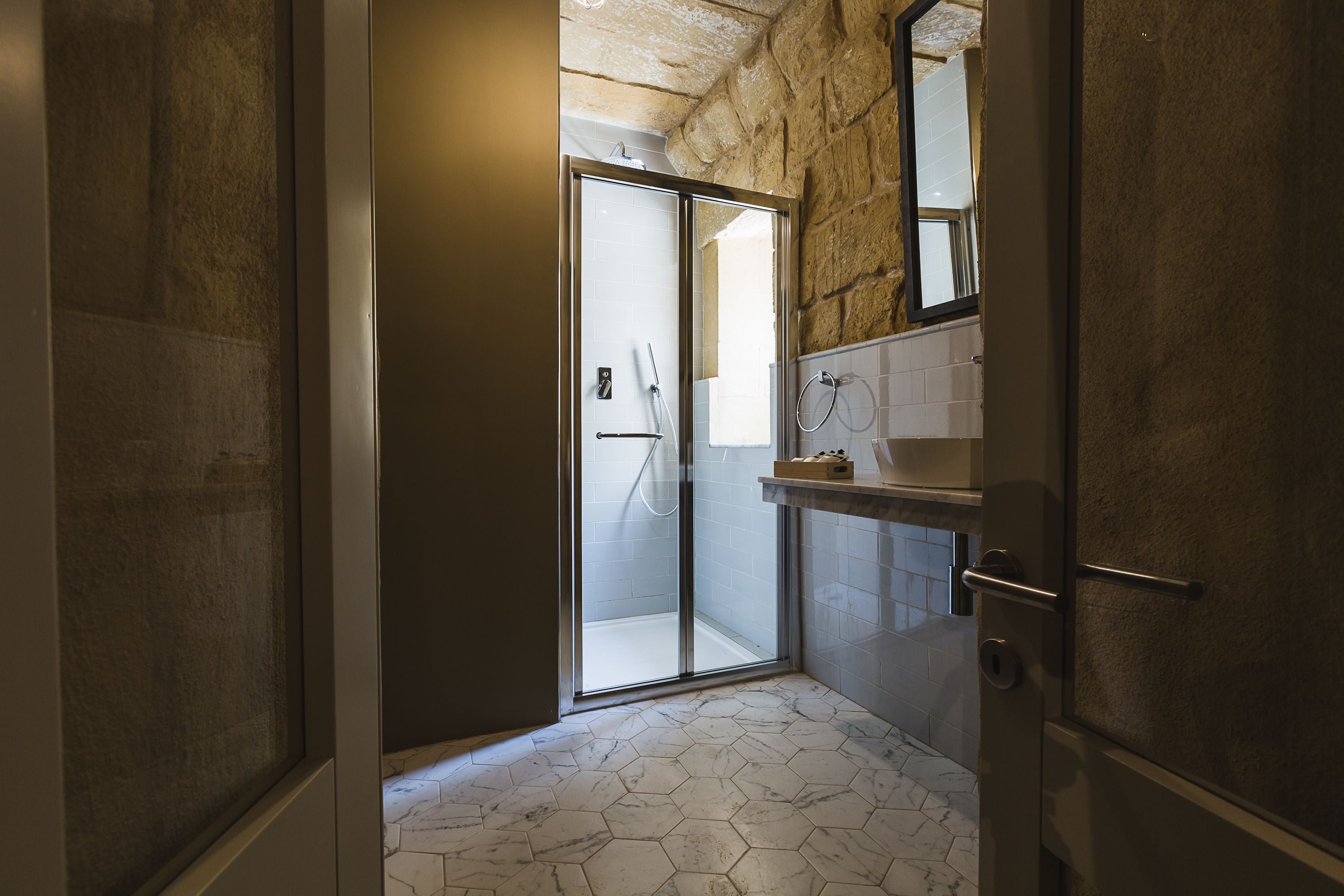 A bathroom with a glass shower door, a marble floor, and a stone wall.