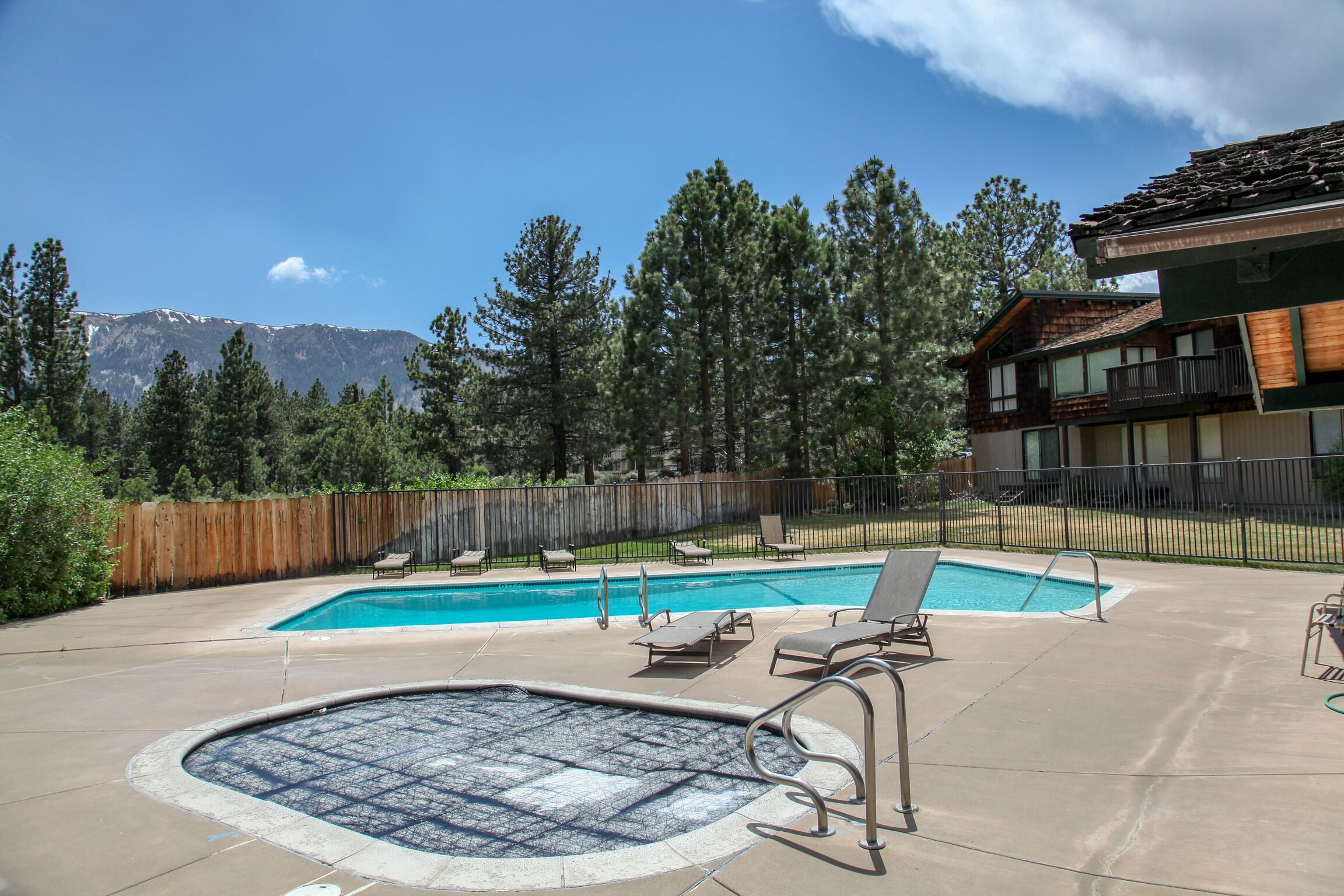 A backyard with a swimming pool, hot tub, and lounge chairs.