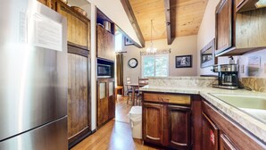 Una cocina con armarios de madera, un refrigerador de acero inoxidable, una cafetera y un comedor con mesa y sillas.