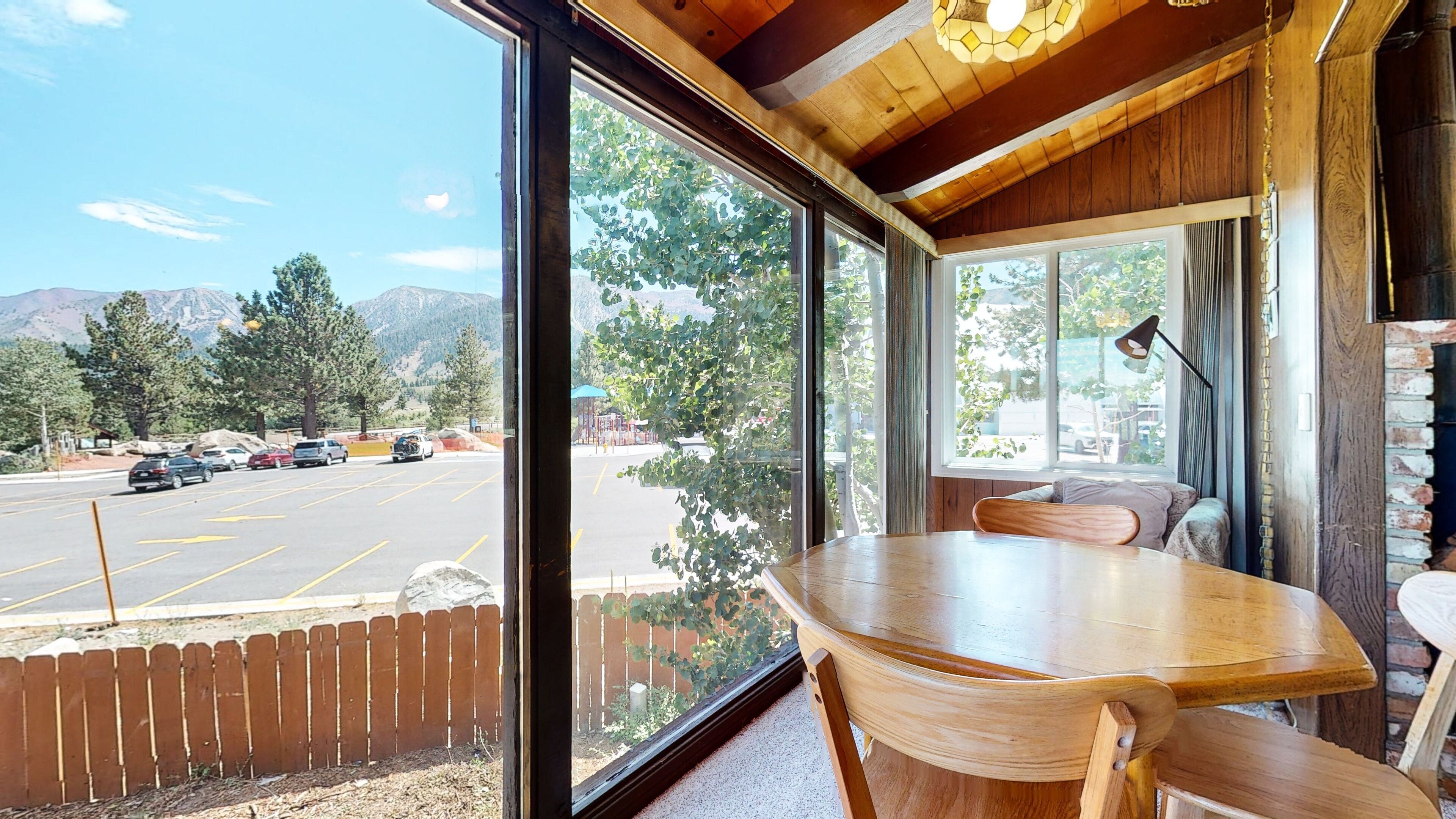 A wooden dining area with a large window overlooking a parking lot and mountains.