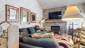 A cozy living room with a stone fireplace, a television mounted above it, and a large floor lamp.