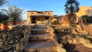 Un sendero de piedra que conduce a un edificio con tejado de azulejos y un gran árbol en primer plano.